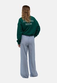 Sweat-shirt vert avec "ATHLETICS MINDS" en texte blanc au dos, associé à un pantalon à larges jambes bleu et blanc à rayures, avec une texture lisse.