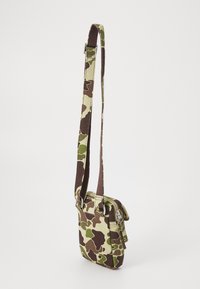 Kamakóvaná crossbody taška v zelenej a hnedej látke s uzáverom na zips, nastaviteľným popruhom a prednou vreckom na klopu. Hladký povrch.