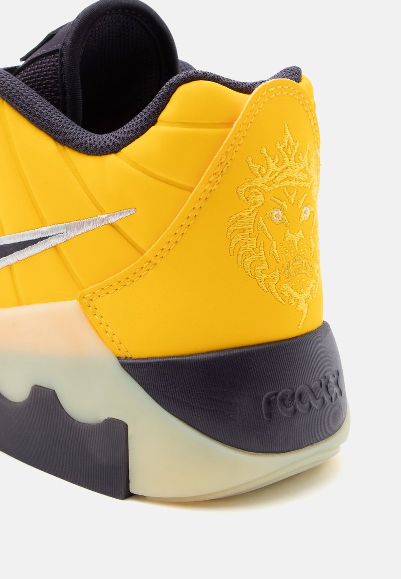 Yellow sneaker with textured rubber sole, stitched accents, and a lion emblem on the heel. Features a grey sock liner and logo detail.