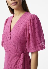 Roza haljina s voluminoznih rukavima, s rupicama u tkanju, teksturiranim materijalom i detaljem vezivanja u struku. Elegantna izreza i prozračan dizajn.