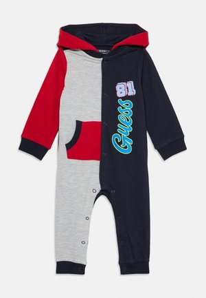 Combinaison à capuche pour enfant avec panneaux rouges, gris et bleu marine, poche avant, boutons-pression et "Guess 81" imprimé sur le côté bleu marine.