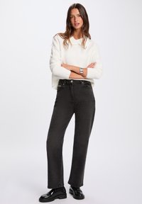 Jeans neri a vita alta con una vestibilità dritta, abbinati a un maglione bianco in maglia, con polsini a coste e scollatura rotonda.