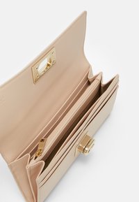 Portafoglio in pelle beige con chiusura dorata, dotato di due scomparti e una tasca con zip, texture liscia e dettagli cuciti.