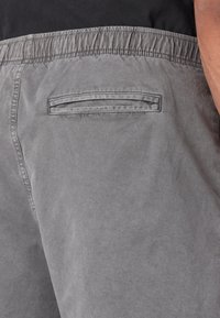 Shorts gris avec une ceinture élastique et une seule poche arrière. Le tissu a une texture douce et un aspect légèrement usé.