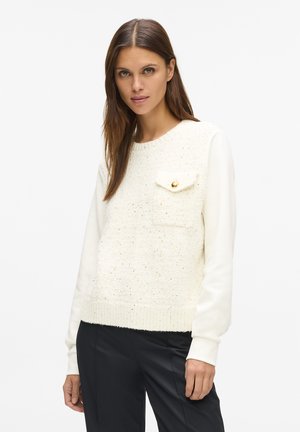 Gestrickter Pullover mit einem strukturierten elfenbeinfarbenen Körper und glatten cremefarbenen Ärmeln. Verfügt über eine Brusttasche mit goldfarbenem Knopfakzent und einem gerippten Saum.