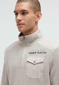 Hellegrauer, mit Reißverschluss versehenen Pullover aus strukturiertem Stoff, ausgestattet mit einer Brusttasche, besticktem Branding und einem hohen Kragen.