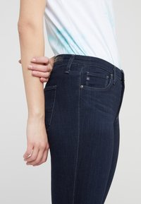Mörka denimskinnyjeans med en åtsittande design. Funktioner inkluderar fram- och bakfickor, kontrasterande sömmar och en märkestagg i midjan.
