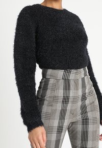 Black fluffy sweater with long sleeves, paired with high-waisted gray plaid trousers featuring striped patterns and textured fabric.