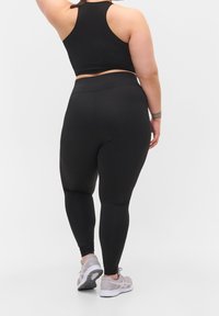 Black athletic crop top and fitted leggings made of stretchy fabric, featuring a smooth texture and minimal seams. Grey sneakers with mesh accents.