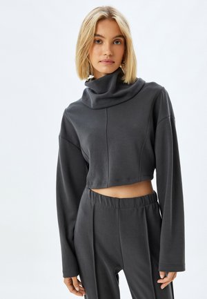 Sudadera corta de color gris oscuro con cuello vuelto, mangas largas y una textura suave. Combinada con pantalones de talle alto en gris oscuro a juego.