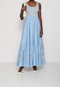 Ljusblå maxikjol med broderade blommönster, vadderad midja och lagerkant, ihop med en åtsittande grå tanktop och vita klackar.