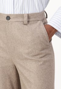 Beige wool trousers featuring a smooth texture, straight leg design, and a front pocket with a single black button at the waistband.