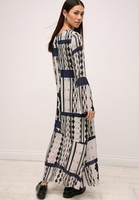 Robe longue et fluide en tissu léger, avec des motifs géométriques noirs et marine sur un fond beige. Manches longues et décolleté rond.