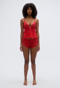 Ensemble de lingerie en dentelle rouge comprenant un haut à col en V avec bordure en dentelle et un short assorti en dentelle. Tissu lisse avec motifs floraux et bords festonnés.