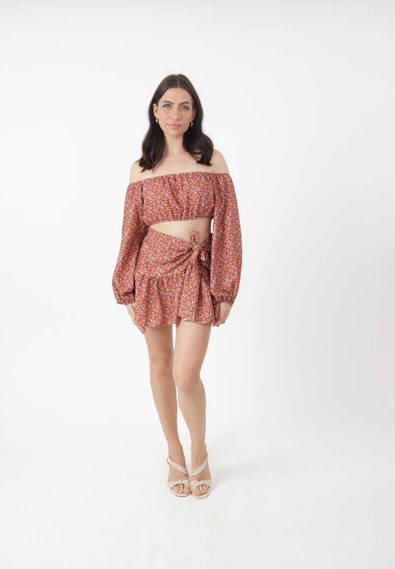 Top corto floral sin hombros en color óxido con mangas largas, combinado con una falda envolvente a juego que presenta un acento atado y un dobladillo rizado.