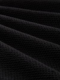 Zbliżenie na czarną wełnianą tkaninę o miękkiej, prążkowanej fakturze i widocznym wzorze dzianiny w przekątnych fałdach.