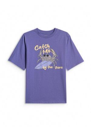 Fioletowa koszulka z krótkim rękawem z krabem w okularach przeciwsłonecznych trzymającym deskę surfingową oraz żółtym napisem „Catch Me by the Shore”.