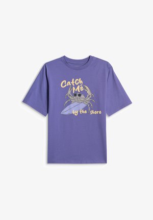 Fioletowa koszulka z krótkim rękawem z krabem w okularach przeciwsłonecznych trzymającym deskę surfingową oraz żółtym napisem „Catch Me by the Shore”.
