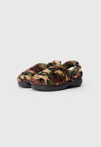 Chaussons à enfiler avec un motif camouflage flou, semelles noires et sangles ouvertes à l'arrière sur un fond gris clair uni.