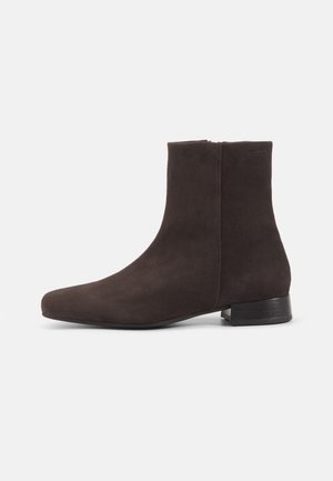 Brune suède ankelstøvler med en glat tekstur, spids tå og en lav, rektangulær sort hæl; har et slankt, minimalistisk design.