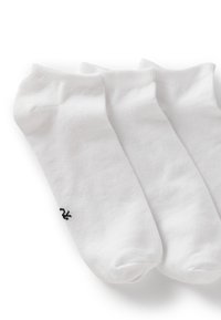 Calzini bianchi in cotone alla caviglia, tre paia esposti. Presentano bordi a coste e un piccolo logo nero su un calzino. Texture morbida, design semplice.