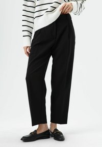 Zwarte, op maat gemaakte broek met een hoge taille en een rechte pijp. Gecombineerd met een wit gestreepte trui en zwarte loafers.