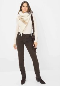 Lichte lange mouwen top, gecombineerd met donkerbruine broek en een zachte, gemusterde crème- en bruine sjaal. Bruine tas met franjes voegt detail toe.