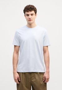 Světle modré bavlněné tričko s krátkým rukávem a volnějším střihem; minimalistický design s jemným logem na hrudi.
