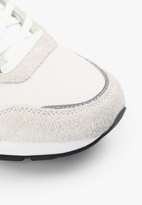 Zapatilla de deporte gris claro con una punta de ante texturizado, parte superior de malla, cordones blancos y suela de goma negra con un diseño aerodinámico.