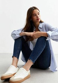 Zapatillas blancas y beige con una suela texturizada, combinadas con unos jeans skinny azul oscuro con dobladillos deshilachados y una camisa de botones a rayas azules.