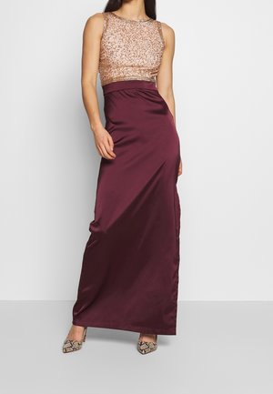 Woman wearing sleeveless gold sequin top with high-waist dark purple satin floor-length skirt and snakeskin high heels.