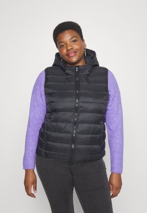 Gilet matelassé noir avec fermeture éclair et capuche ; présente des coutures horizontales. Associé à un pull violet à manches longues et un jean foncé.