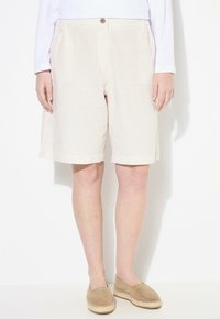 Béžové pruhované šortky s knoflíkovým zapínáním, volný střih a ohrnuté manžety. V kombinaci s hnědými espadrilkami.