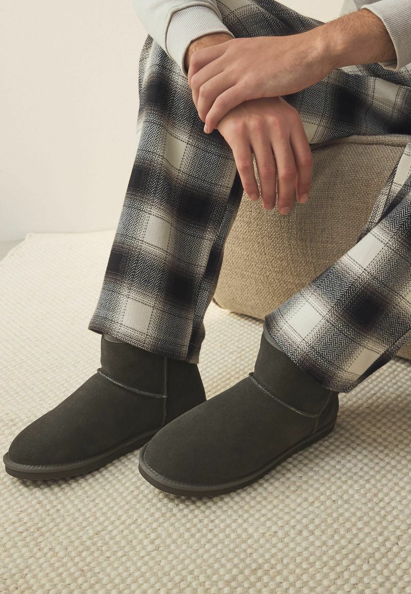 Stivali alla caviglia in suede grigio scuro con una texture morbida, caratterizzati da un design semplice e cuciture decorative, abbinati a pantaloni a quadri.
