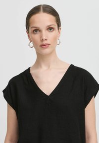 Top in lino nero con maniche corte arrotolate e scollatura a V, caratterizzato da una vestibilità comoda e una consistenza liscia. Nessun motivo o accessorio notevole.