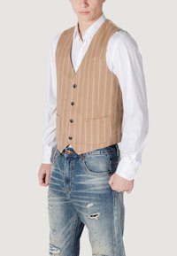 Gilet a righe beige in tessuto, con colletto a punta, cinque bottoni e due tasche frontali, abbinato a jeans blu strappati.