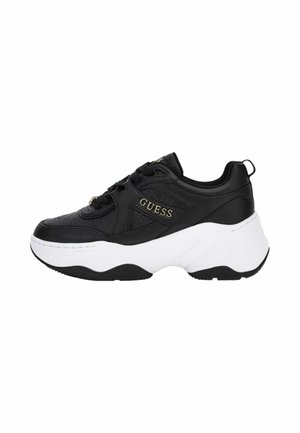 Baskets noires Guess avec semelle blanche épaisse, motif embossé, fermeture à lacets à l'avant et logo doré "GUESS" sur le côté et la languette.
