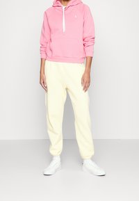 Rosa hoodie med framficka och vit dragsko, i kombination med gula sweatpants och vita sneakers. Avslappnad, bekväm passform.