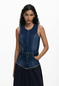 Denim jumpsuit with a fitted bodice, zip closure, and a belted waist. Features contrasting stitching and a frayed hemline at the skirt.