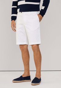 Pantalones cortos de algodón blancos con un frente plano, bolsillos laterales y un ajuste entallado. Lleva unos espadrilles azul marino con suela de yute.