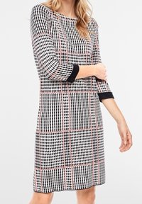 Robe à motifs noir et blanc avec des accents roses, manches trois-quarts, encolure ronde et coupe droite, dotée d'un tissu texturé.