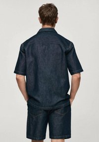 Ciemnoniebieska koszula jeansowa z krótkim rękawem w zestawie z pasującymi szortami. Charakteryzuje się ozdobnym przeszyciem i luźnym krojem, z klasycznym kołnierzykiem.