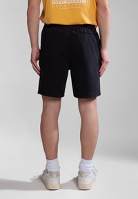 Pantalones cortos de color navy con un corte relajado, que cuentan con una cinturilla elástica. Combinados con zapatillas blancas y calcetines cortos blancos, vistos desde atrás.