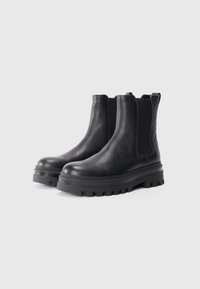 Bottes noires en cuir jusqu'à la cheville avec une surface texturée, des panneaux élastiques sur les côtés et une semelle en caoutchouc épaisse avec un motif de semelle robuste.