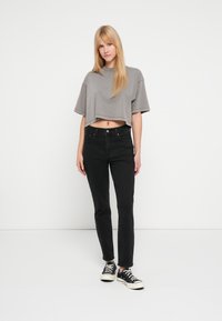 Camiseta gris recortada con mangas cortas, combinada con jeans ajustados negros y zapatillas negras. Diseño simple, sin patrones ni detalles visibles.