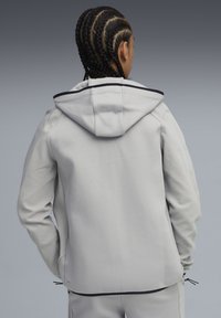 Lys grå hoodie med lynlåsdesign, ribbet tekstur på ærmerne, kontrasterende sort kant på hætten og justerbar snor i kanten.