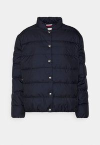 Navy puffer-jakke med høj krave, trykknaplukning, kviltet tekstur og diskret logo-detail på brystet.