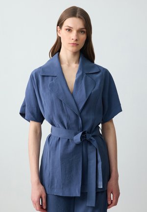 Blaues, kurzärmliges Wickelshirt aus leichtem Stoff mit einem Bindegürtel und großem Schalkragen. Glatte Textur mit minimalen Details.