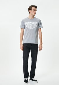 Camiseta de algodón gris con gráfico en blanco que dice "COSMIC", combinada con jeans de mezclilla oscura y zapatillas negras con cordones blancos.