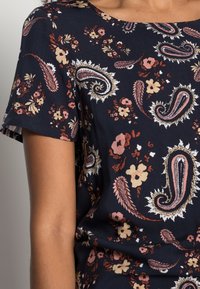 Námořnická modrá tričko s krátkým rukávem s paisley vzorem v krémové, růžové a burgundské barvě. Měkká tkanina s kulatým výstřihem a volným střihem.